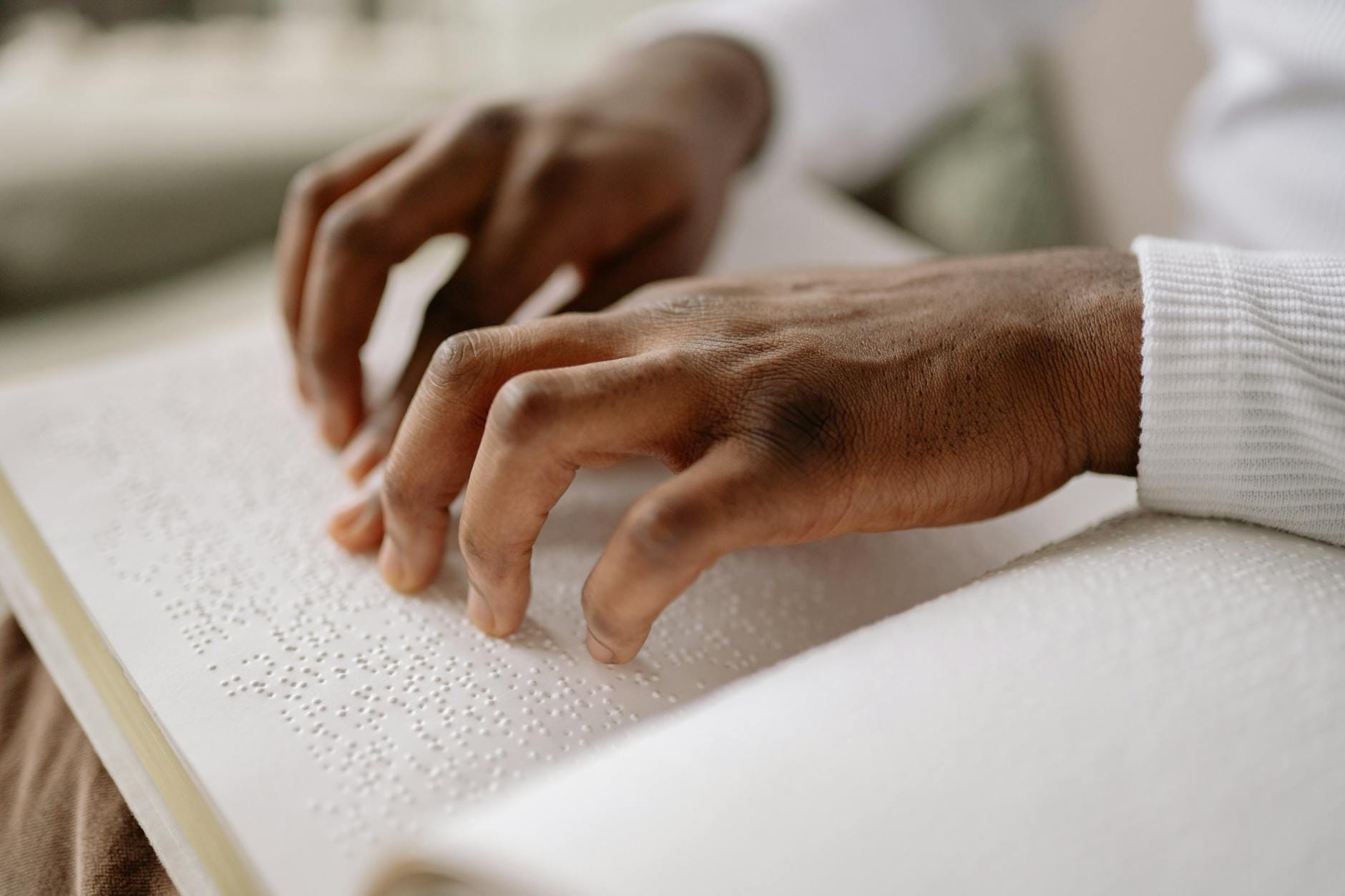 Dłonie czytające książkę w alfabecie Braille’a w dobrze oświetlonym wnętrzu