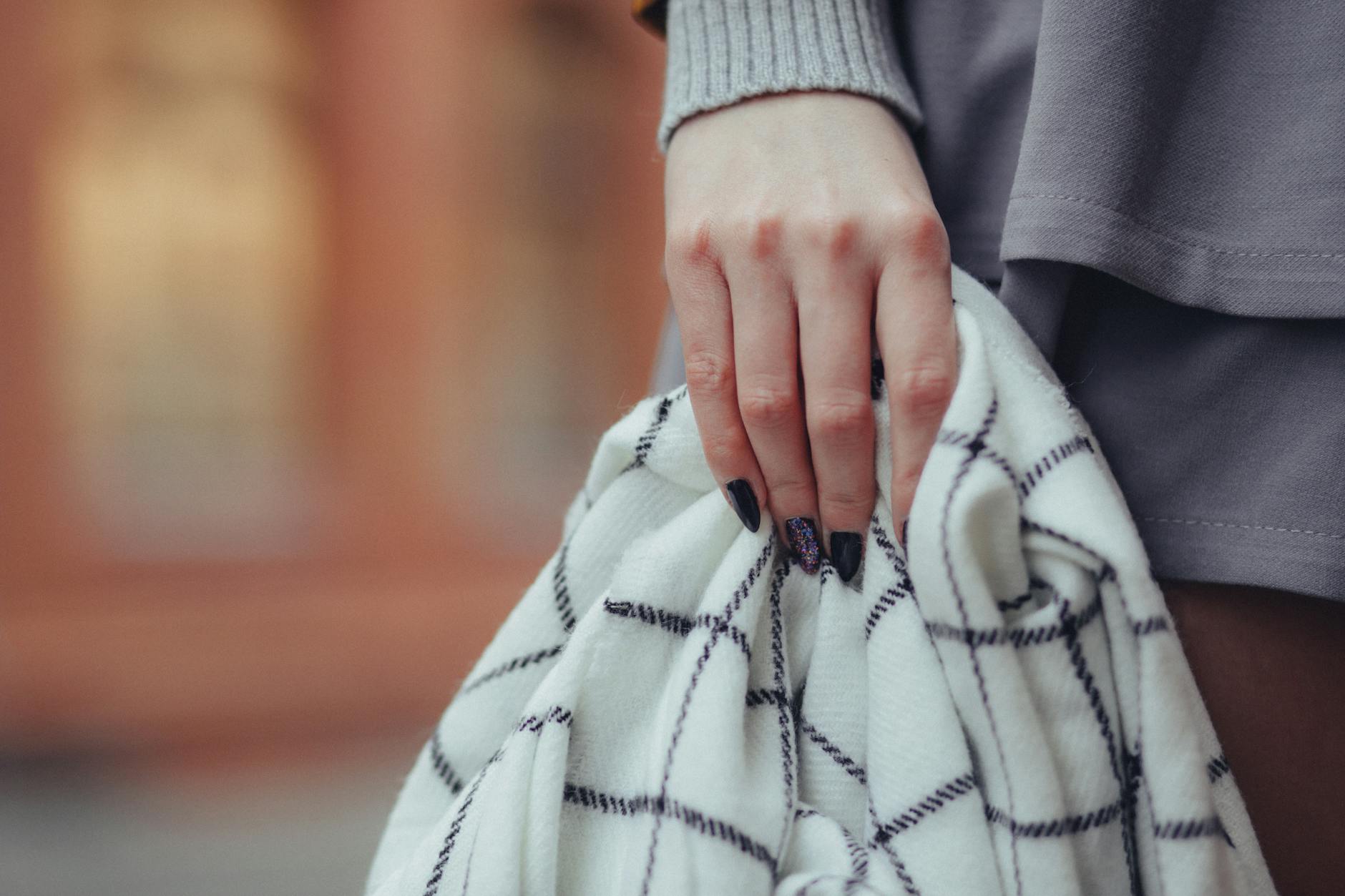 Dłoń kobiety z jesiennym manicure trzymająca wzorzysty koc