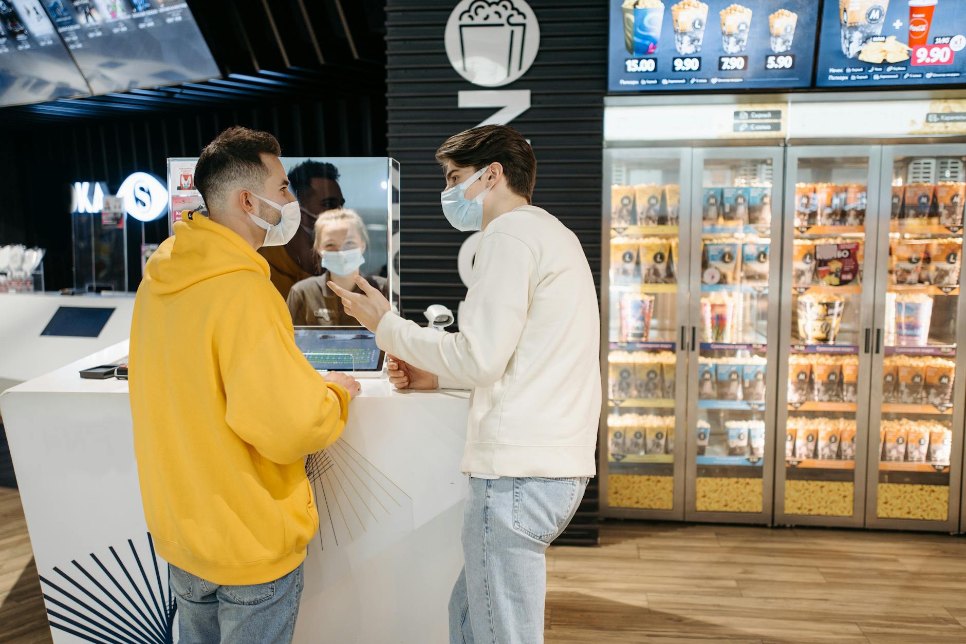 Dwaj mężczyźni w maseczkach kupują popcorn przy ladzie w kinie