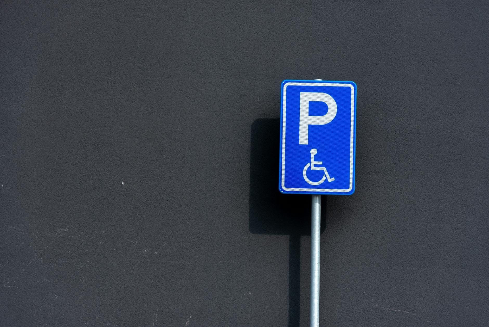 Kiedy brak dostępności cyfrowej można uznać za dyskryminację ze względu na niepełnosprawność Znak miejsca parkingowego dla osób z niepełnosprawnościami na tle ciemnej ściany