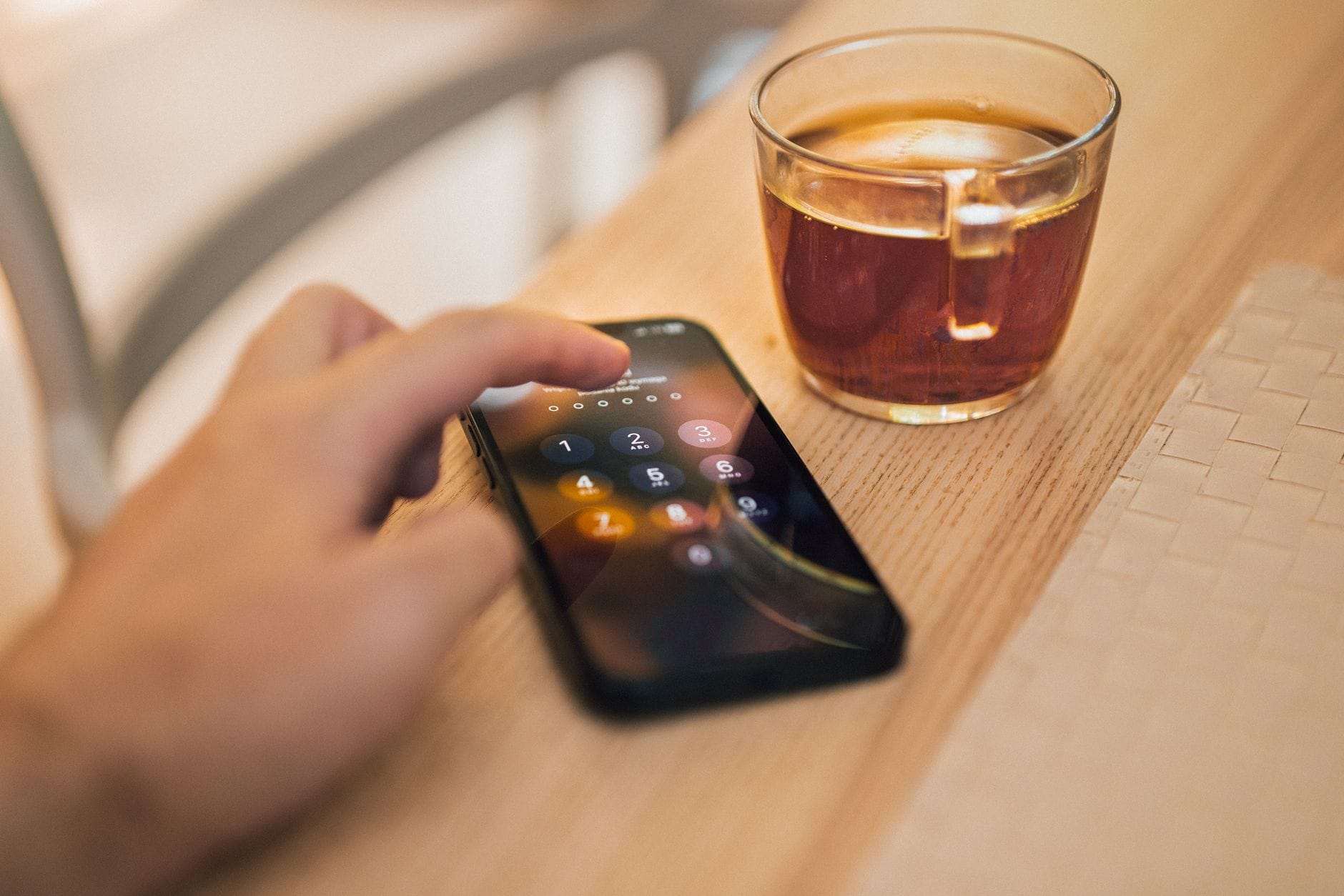 Dłoń odblokowująca smartfon obok filiżanki herbaty na drewnianym stole
