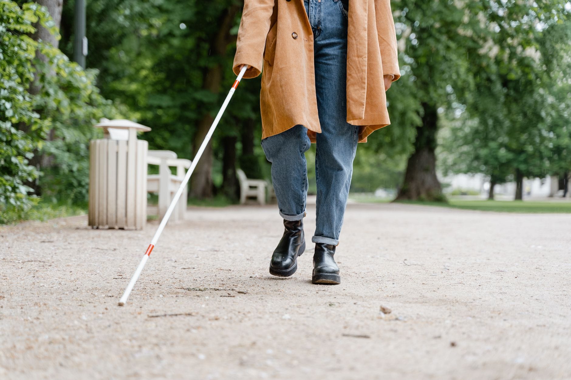 Osoba niewidoma z białą laską idzie przez zielony park