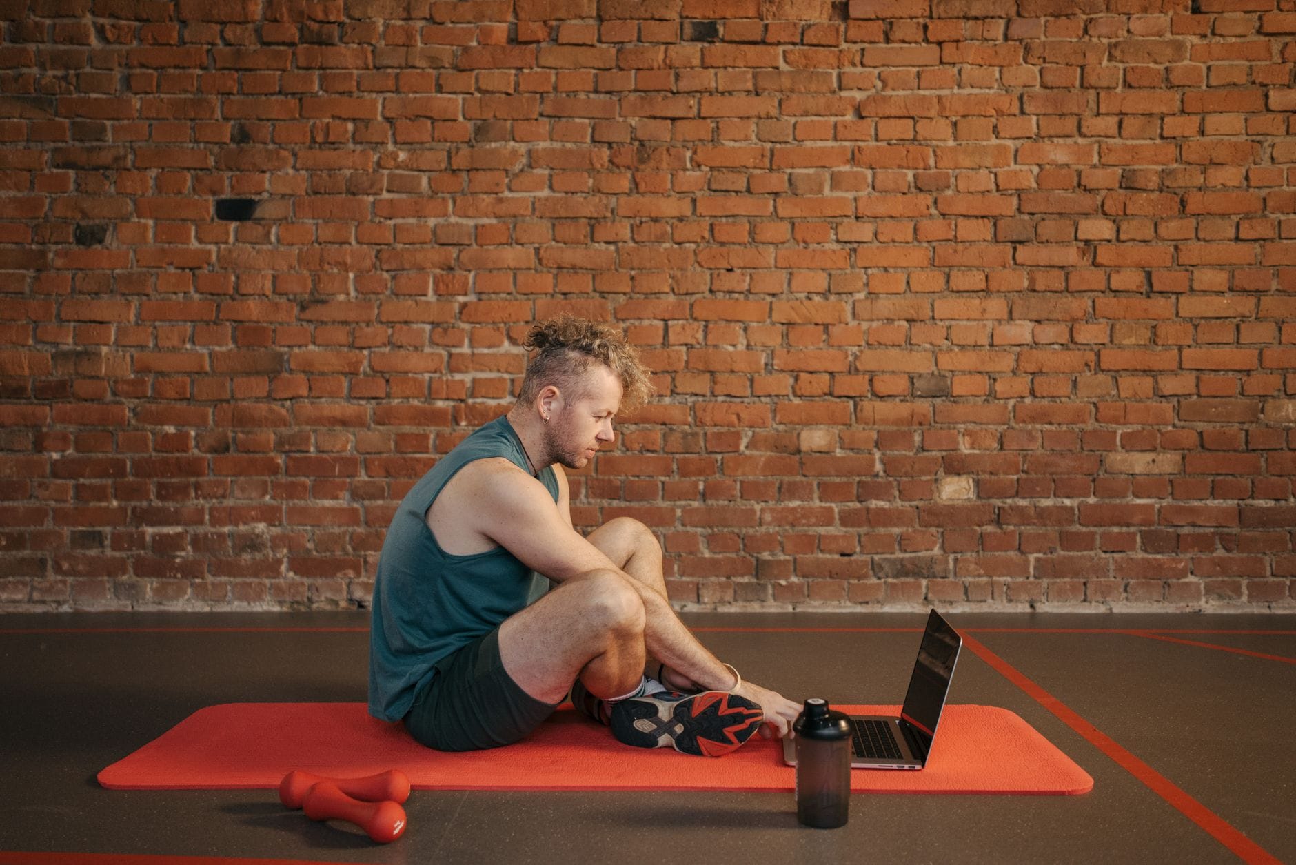 Mężczyzna na macie ćwiczy w domu, korzystając z laptopa z planem treningu