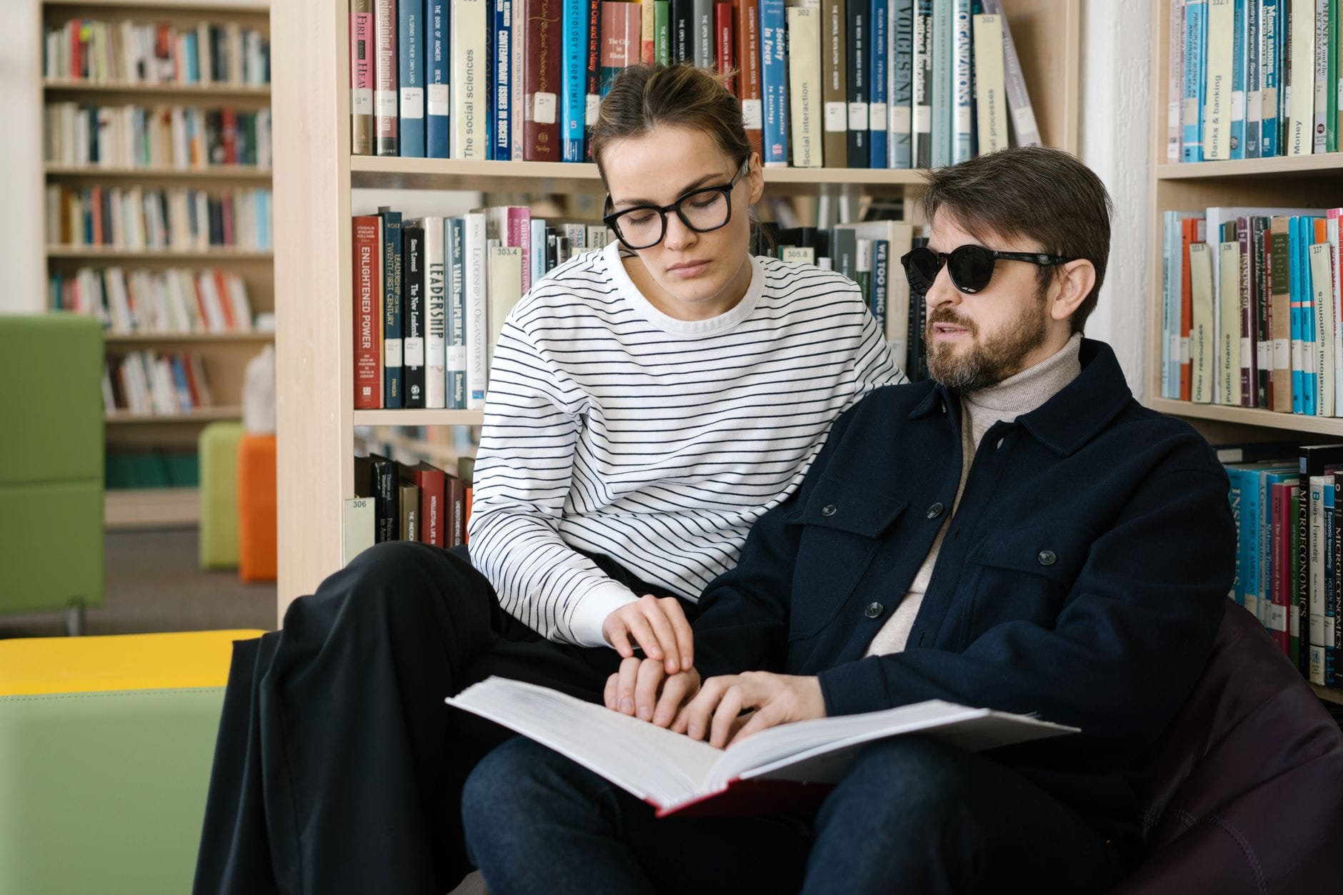 Niewidomy mężczyzna czyta książkę brajlem z pomocą w bibliotece