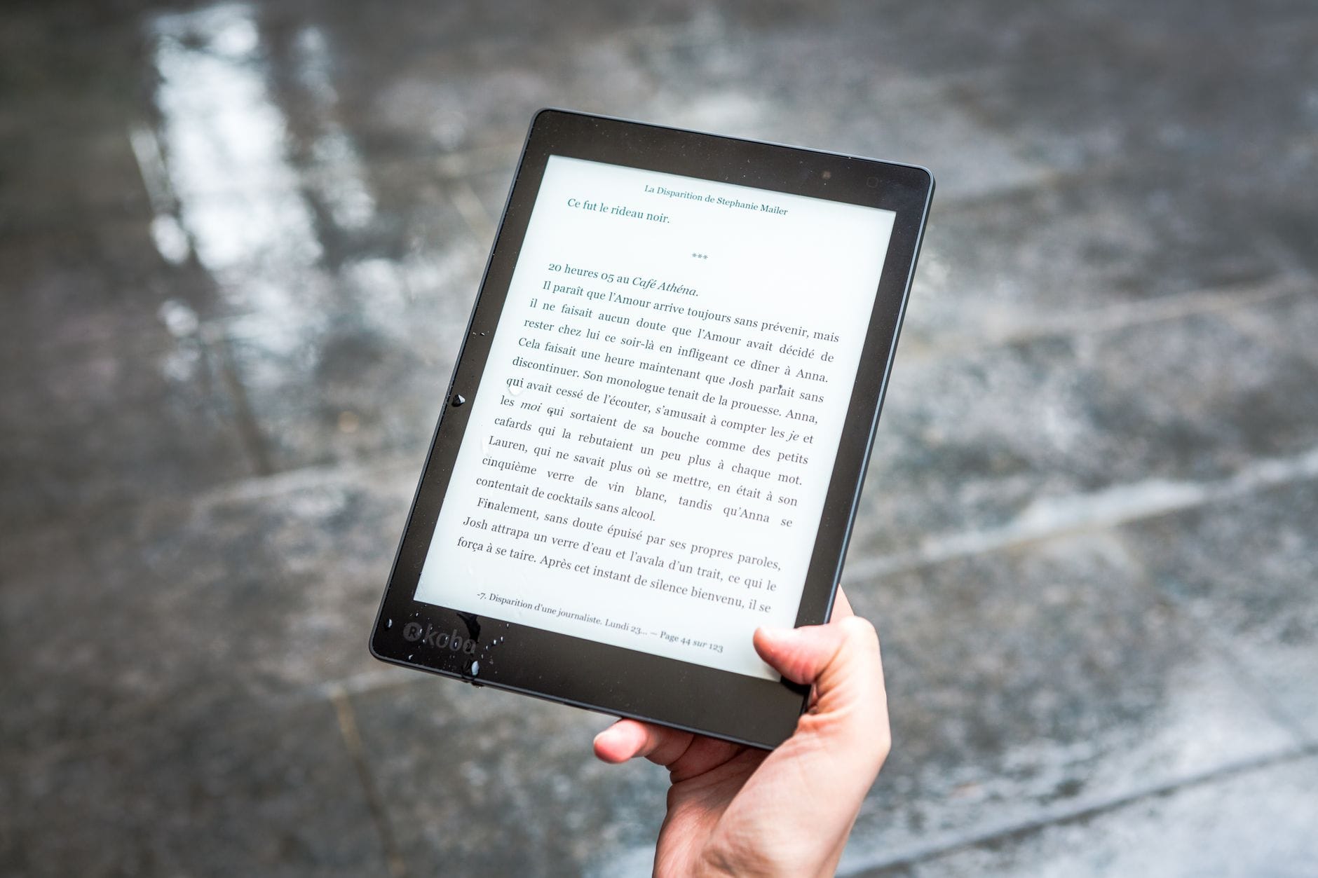 Osoba trzyma czytnik e-booków z tekstem na tle mokrego chodnika
