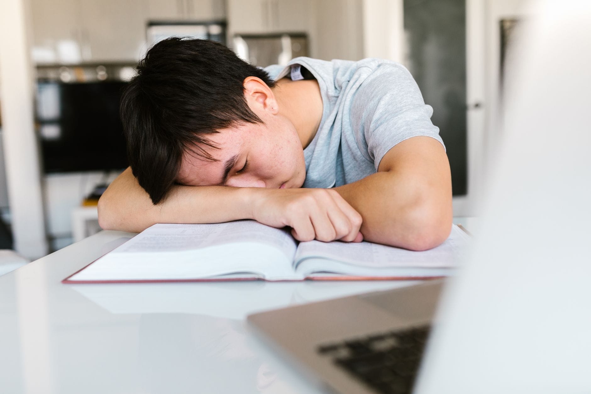 Zmęczony student zasypia nad podręcznikiem przy biurku podczas nauki
