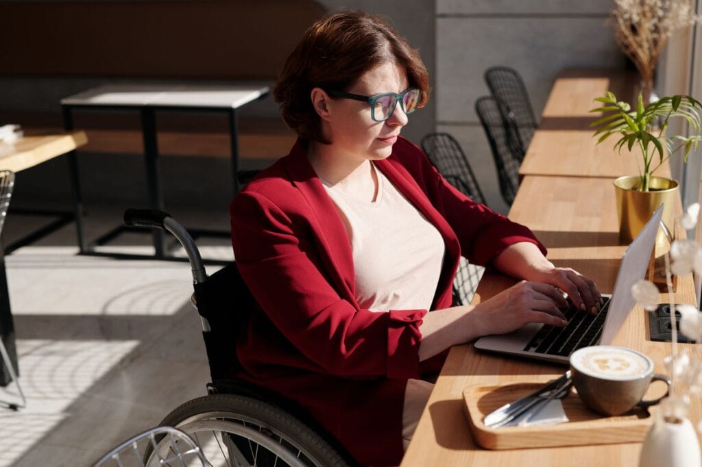 Kobieta na wózku inwalidzkim korzysta z laptopa w kawiarni