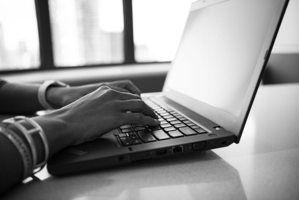 Dłonie piszące na klawiaturze laptopa w czarno-białym zbliżeniu
